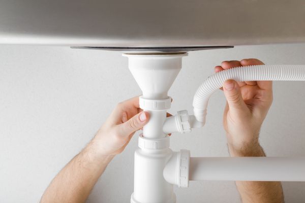 A person installing a dishwasher hose under a sink 