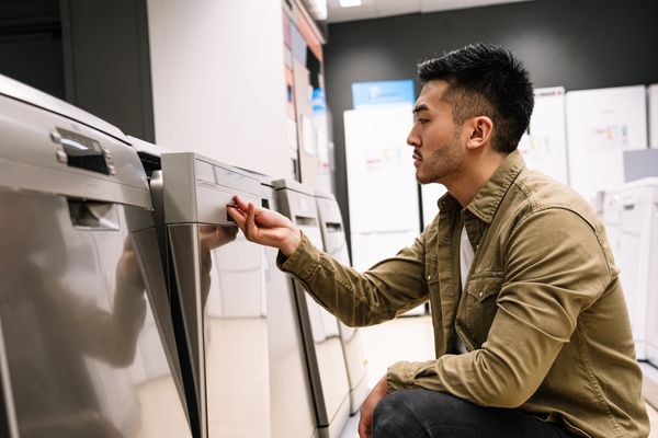 A young man inspecting a dishwasher in a store 
