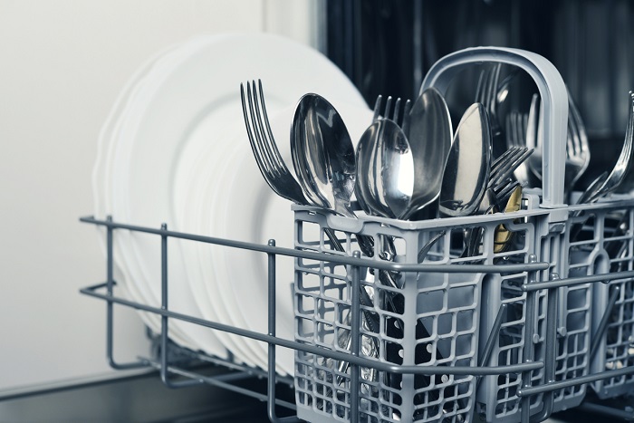 Close up of the bottom rack of a dishwasher that is focused on the clean silverware with white plates in the background.