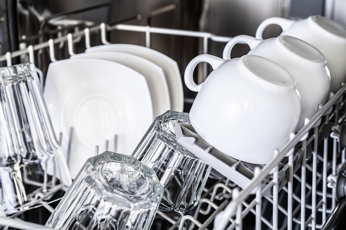 Rows of clean mugs, glasses, and plates loaded up in the top rack of a dishwasher.