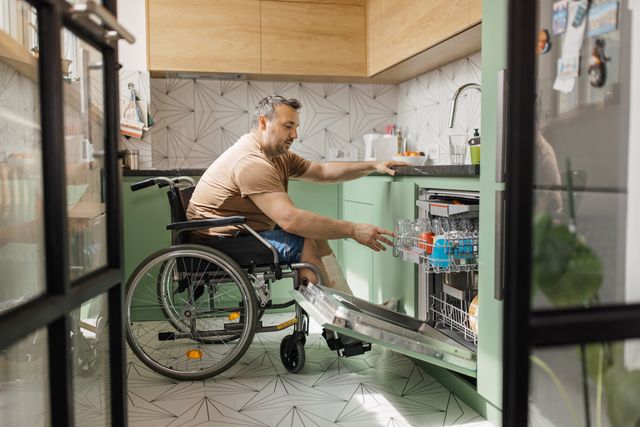front view of a man in a wheelchair loading a dishwasher