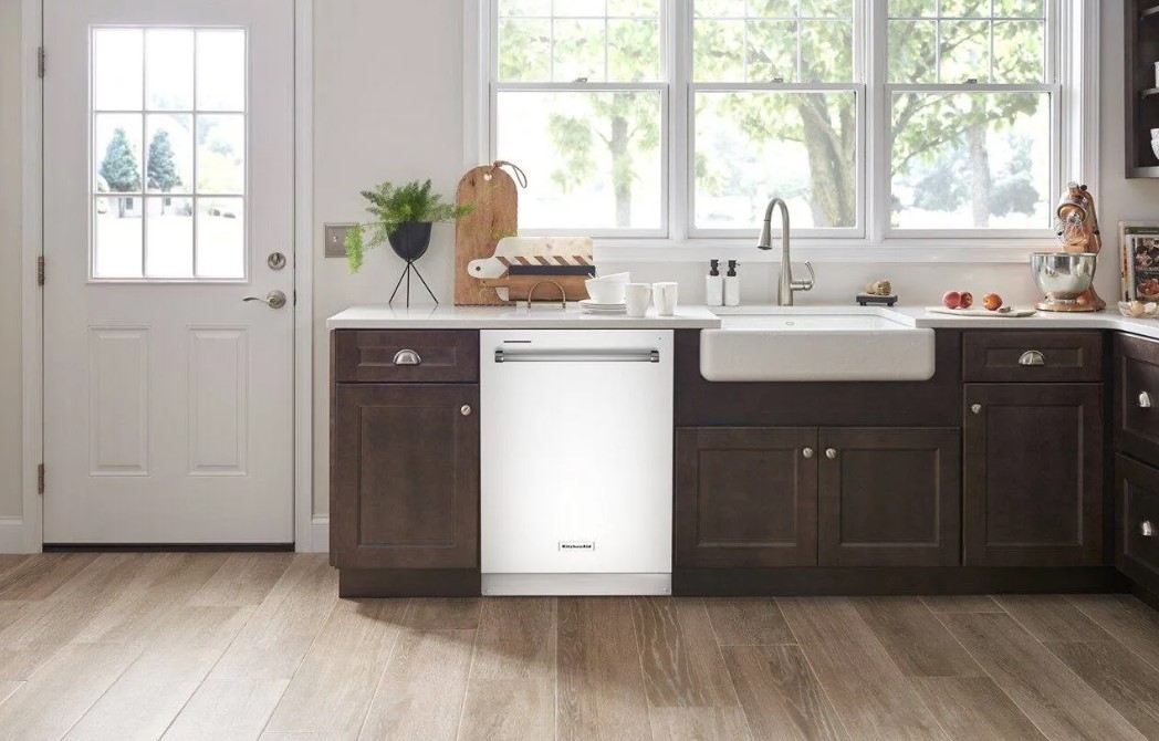 White KitchenAid built in dishwasher installed to the left of a white farmhouse sink