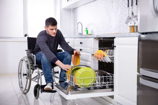 front view of a man in a wheelchair loading a dishwasher