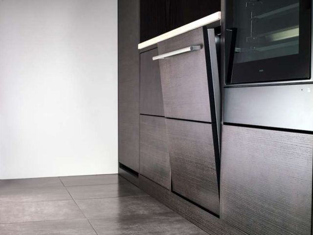 side view of a slightly opened panel ready dishwasher in dark cabinets with silver handles