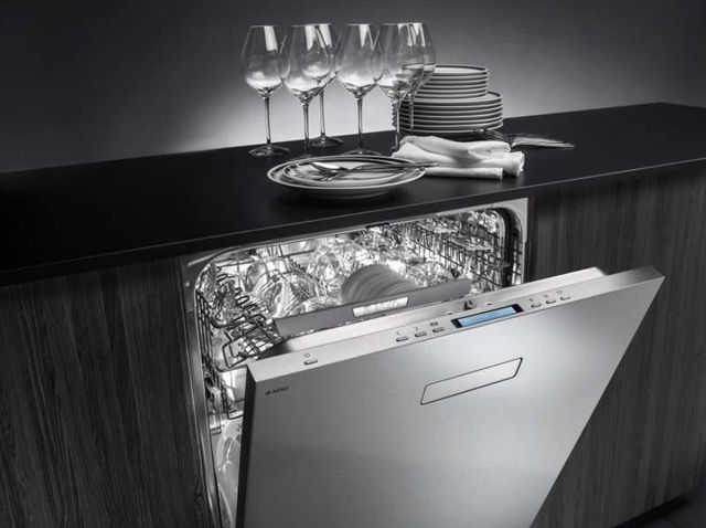 front view of an asko dishwasher, partially opened, with clean glasses and plates on the counter on top, background and countertops are black