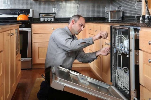 front view of a man unscrewing a dishwasher to fix it