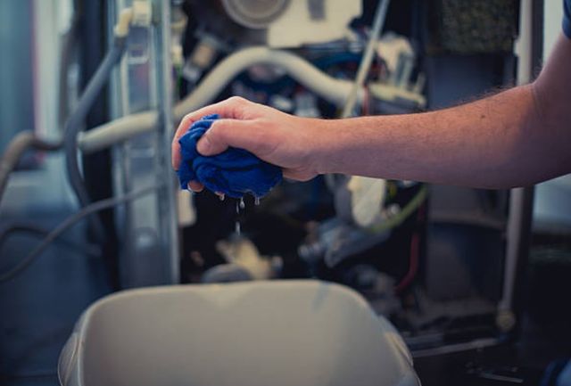 front close view of a hand wringing out a blue rag in front of the back of a dishwasher