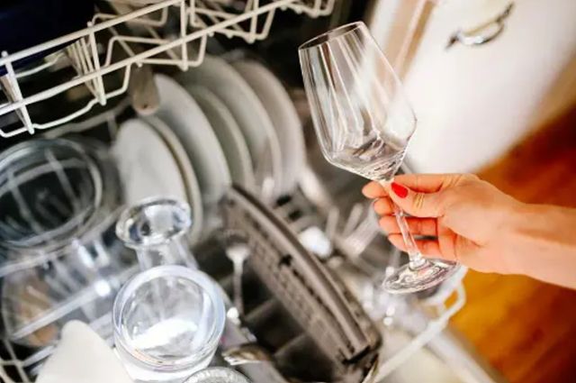 close view of a womans arm pulling a wine glass out of the dishwasher