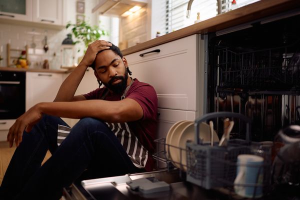 A distressed man sitting next to an open dishwasher 