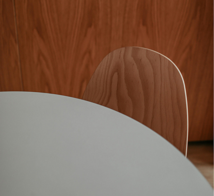 A close-up view of a white, round table with minimalist wood chairs." title="A close-up view of a white, round table with minimalist wood chairs