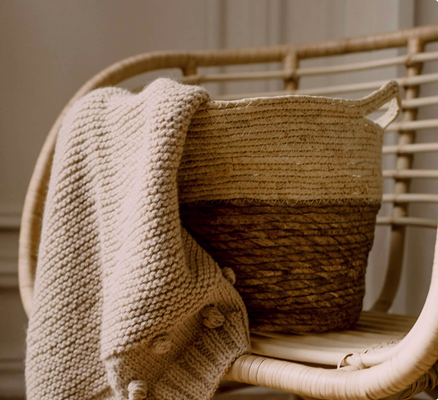 A rattan chair paired with a natural-fiber basket and blanket in varying shades of beige and brown