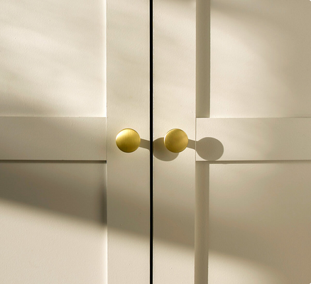A close-up view of a white cabinet with two small, round brass knobs at the center