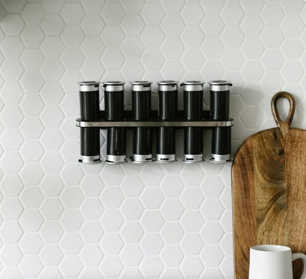 Hexagon-shaped white tile creates a honeycomb pattern backsplash, with a simple spice rack hanging on it