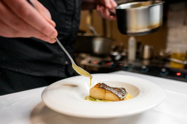A chef drizzing sauce over seared fish 