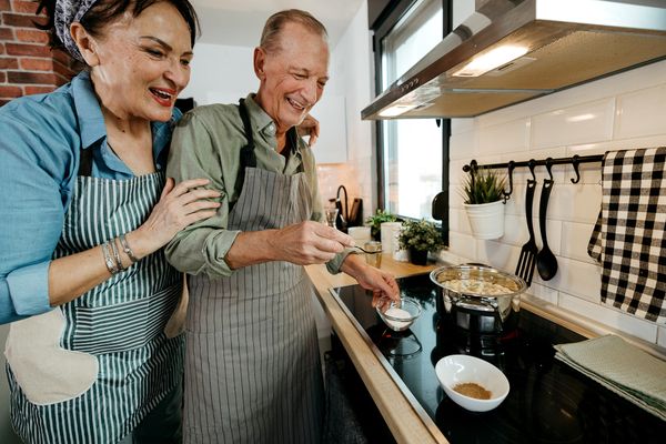 A elderly couple smiling while cooking on a cooktop 
