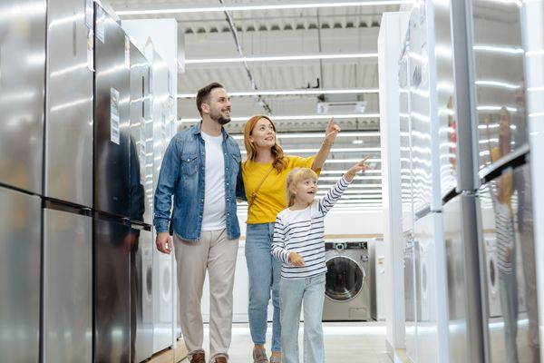 A family of three smiling and pointing at appliances in a store