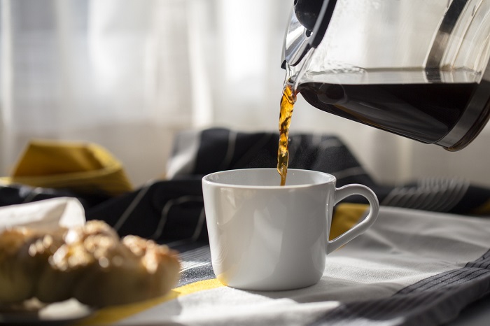 Coffee being poured into cup with breakfast in the background. 