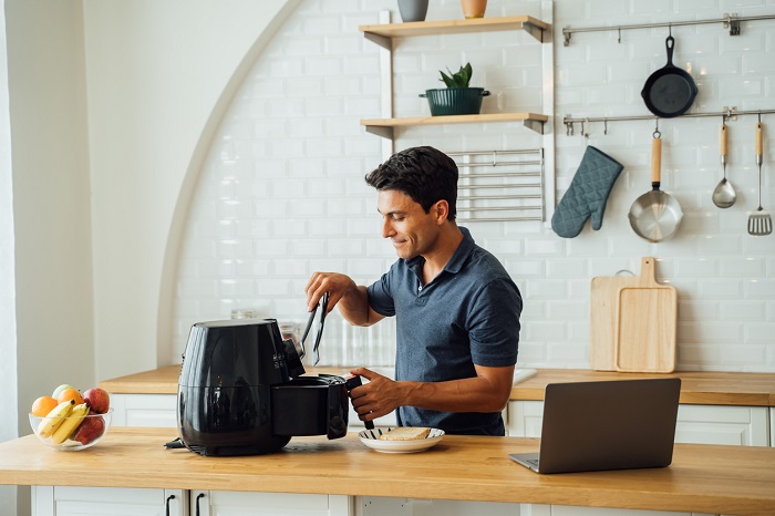 Man using tongs while cooking with air fryer. 