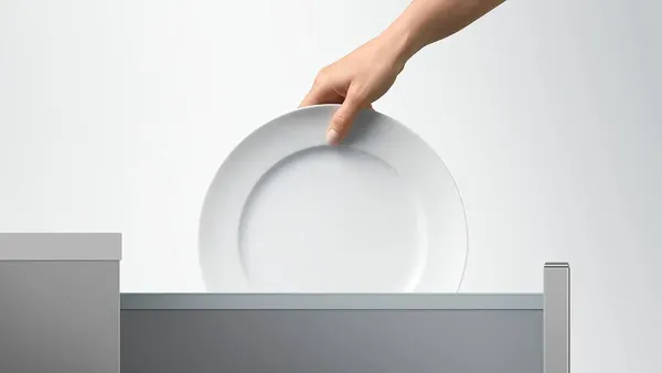 A woman removing a dinner plate from the Fisher & Paykel DD24DV2T9 N dishwasher 
