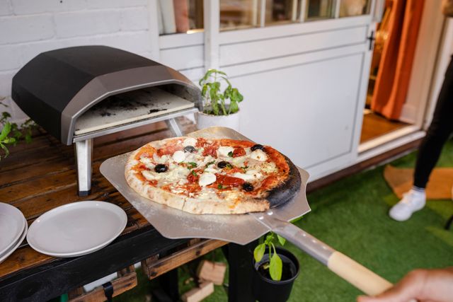 Front view of a person putting pizza in a countertop pizza oven outside