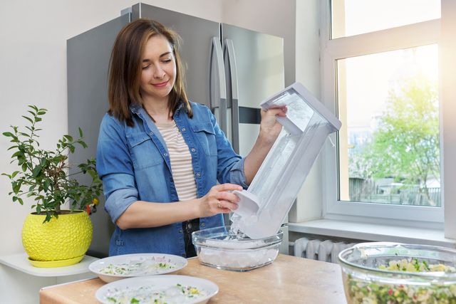 front view of a woman scooping ice from her ice maker into a container