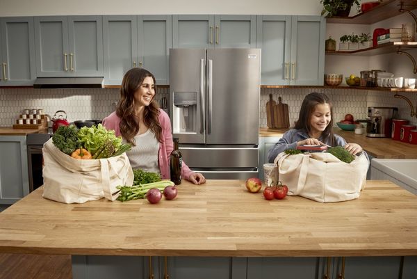 A mother and a child unpacking groceries with a Frigidaire refrigerator in the background