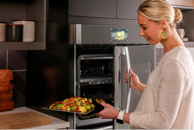 A woman placing items into the GE Profile PTS700LSNSS side swing oven