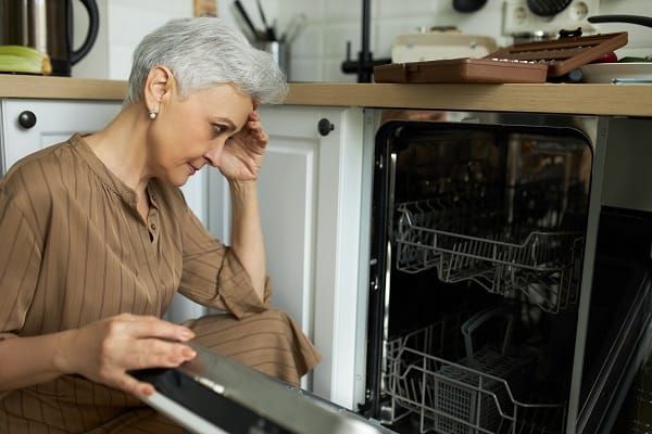 Front view of a woman holding her head and trying to fix her dishwasher not draining