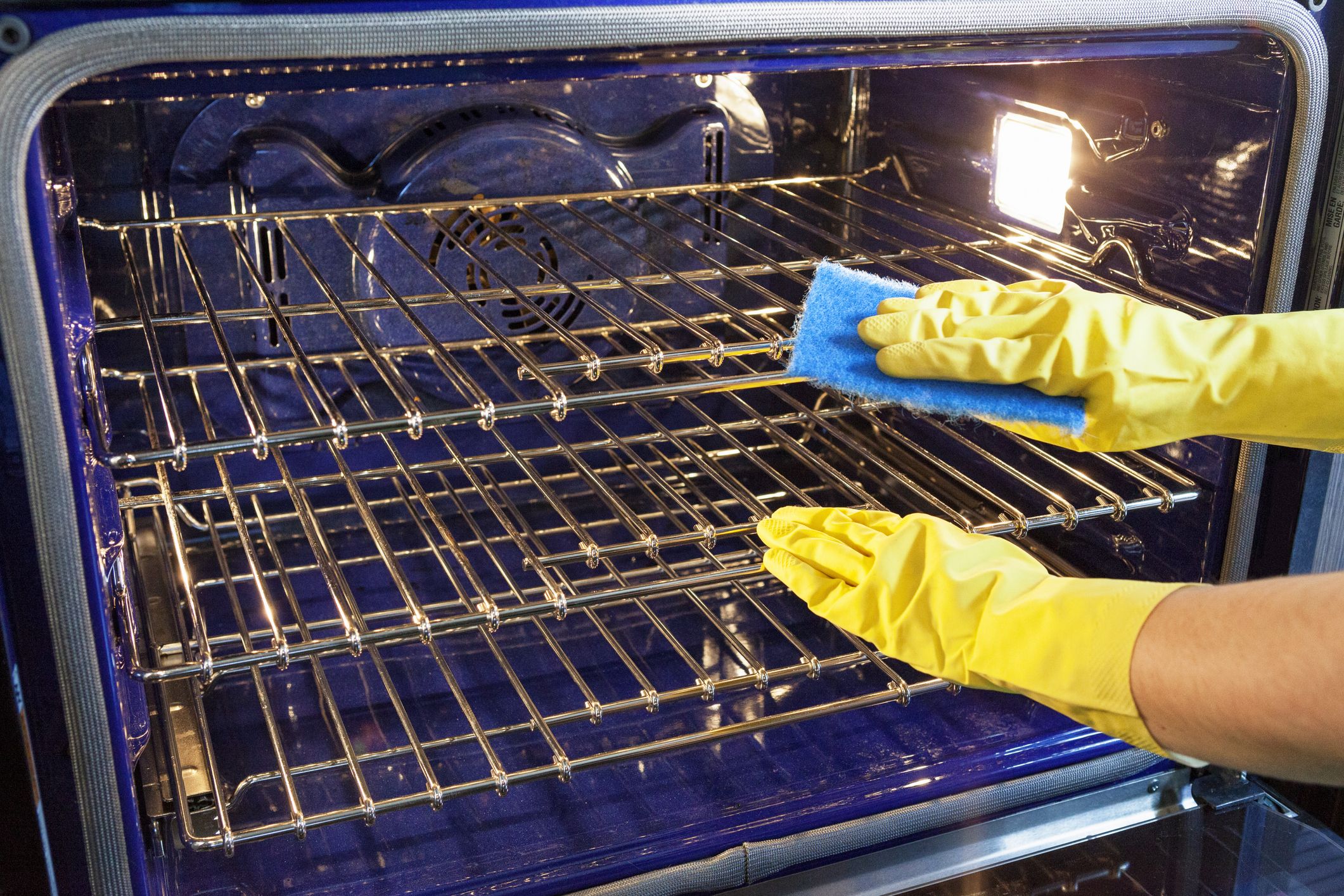 gloved hands cleaning oven racks with sponge