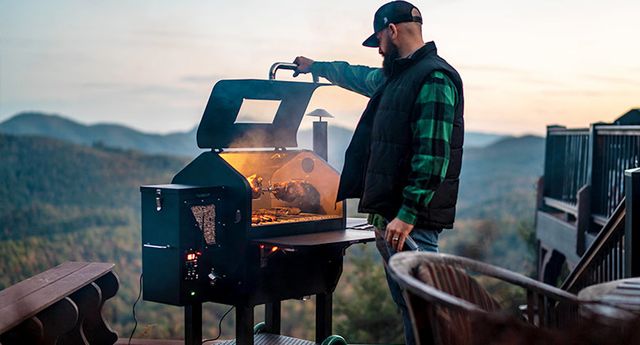 View of a man on a mountain grilling on a wood pellet Green Mountain Grill
