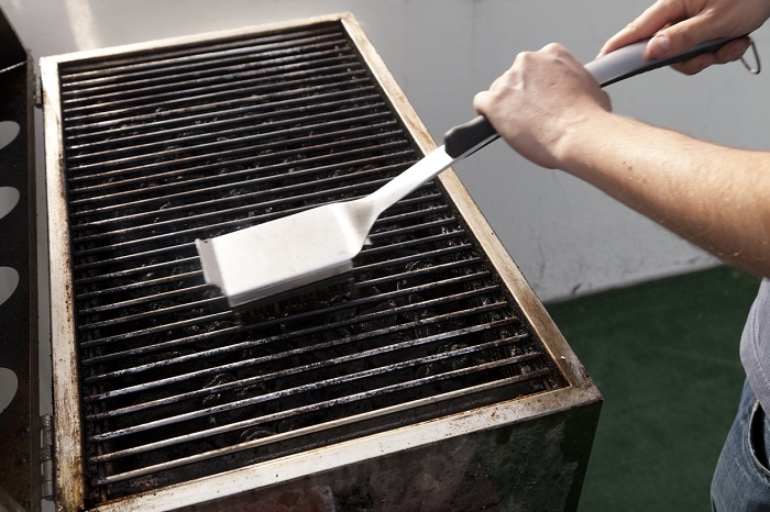 Man cleaning a grill with a grill scrubber.