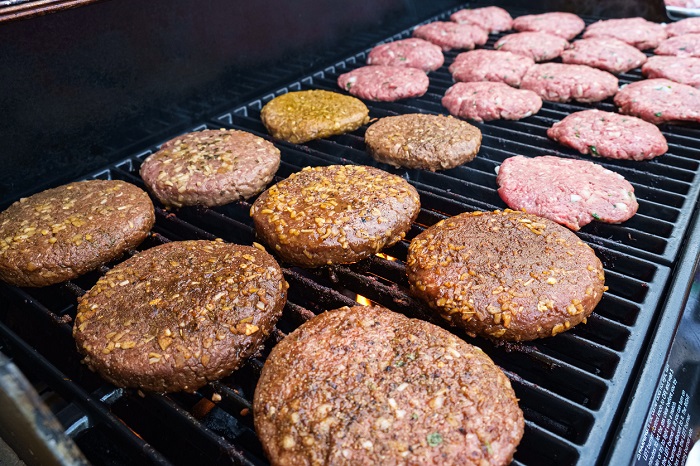 Rows of seasoned burgers on a gas powered grill.