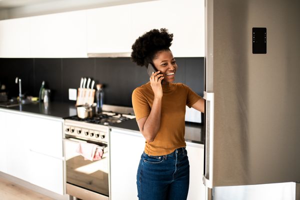 A smiling woman on the phone while using the refrigerator 
