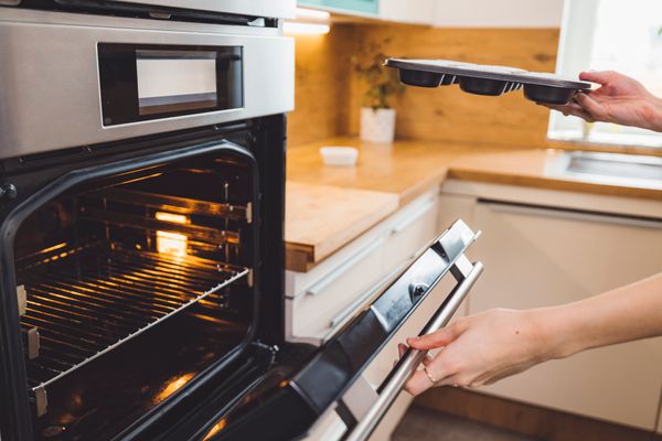 A person inserting a muffin pan into an oven 