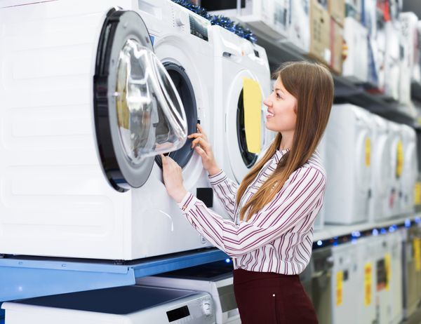 iStock Credit: JackF A young woman inspecting a front load washer in a store