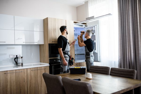 Two appliance technicians installing a built-in refrigerator 