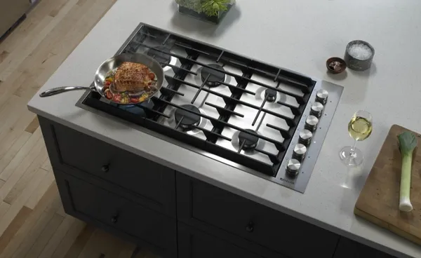The JennAir JGC7636BS gas cooktop with a pan cooking a steak 