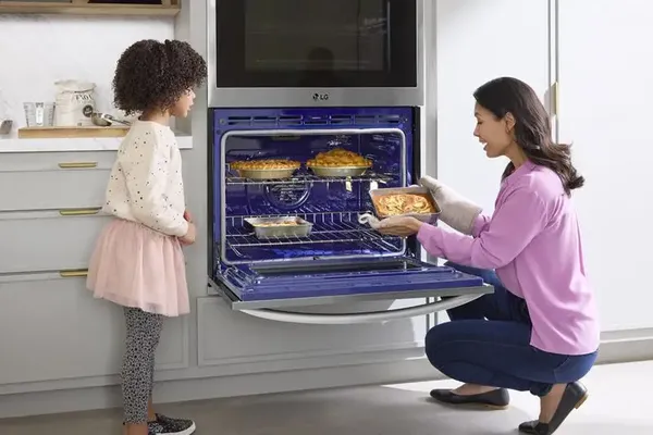 A woman removing an item from the LG WCEP6423F double oven with a child nearby 