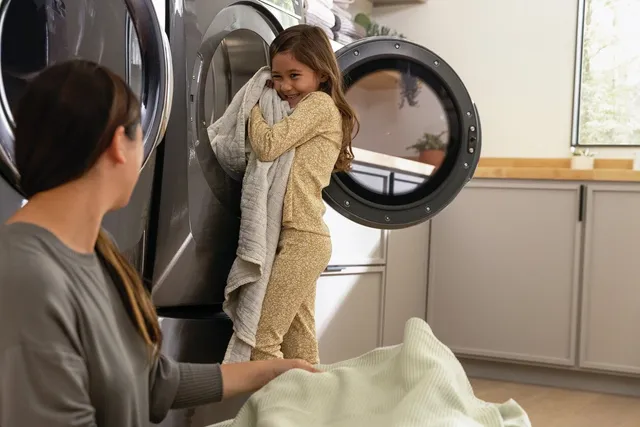 Front view of a child smiling and holding a blanket fresh out of the dryer