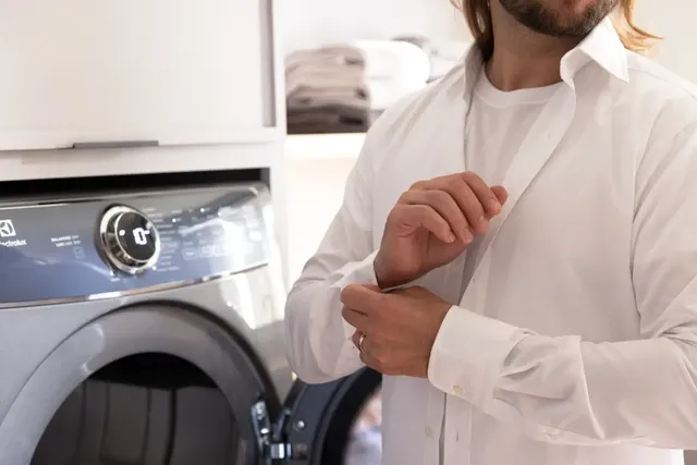 Front view of a man buttoning up a white shirt out of his Electrolux dryer