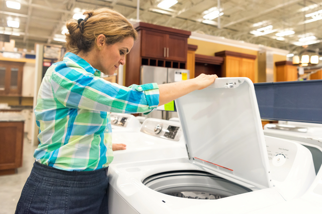 view of a woman looking into a white washing machine in an appliance store