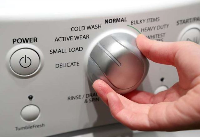 close up view of a hand turning the knob to choose a washer setting