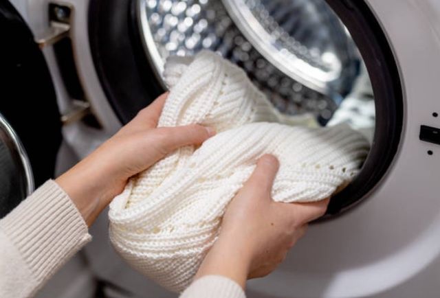 hands putting white wool sweater in a washing machine