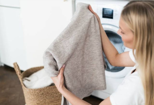 a woman inspecting a wool sweater in front of a washing machine