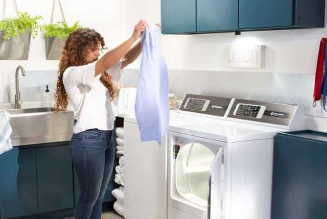 view of a woman pulling clothes out of a speed queen dryer in a white laundry room