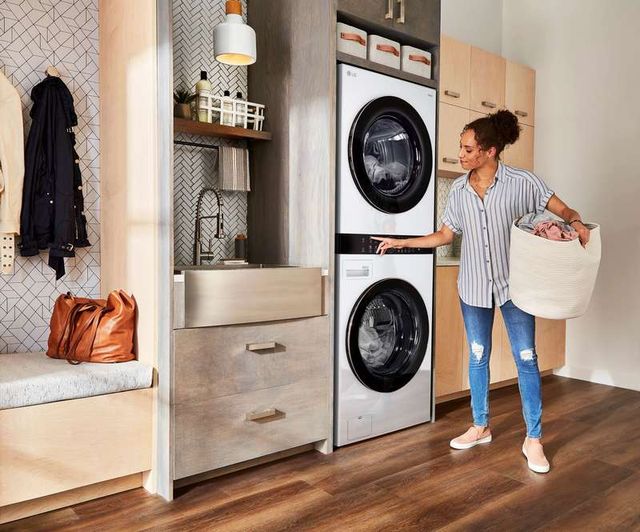 front view of a woman holding a laundry basket in front of a white stackable washer and dryer in a modern laundry room