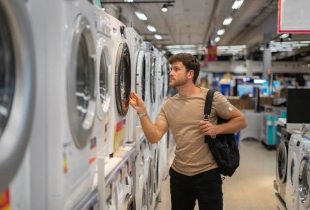 side view of a man looking at one of the dryers in a store aisle of white dryers