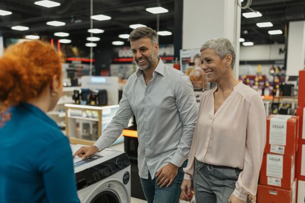 A smiling couple speaking with a sales rep next to a washing machine 