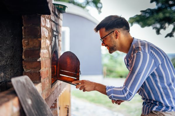 A man opening a wood-burning pizza oven