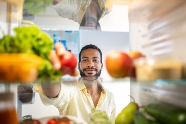 A man reaching for produce inside of a refrigerator 
